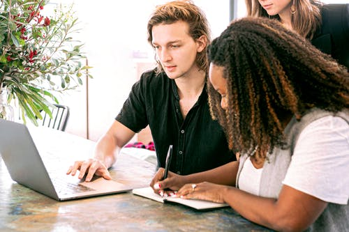 a man working on laptop while woman is taking notes